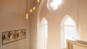 Quarto com janelas em arco, luminária com lâmpadas aparentes e um objeto decorativo fixado na parede.