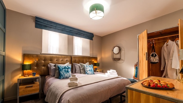 Ein Hotelzimmer mit Bett, Nachttischen, einer Holzkommode, einem Spiegel und einem Fenster mit Vorhängen.