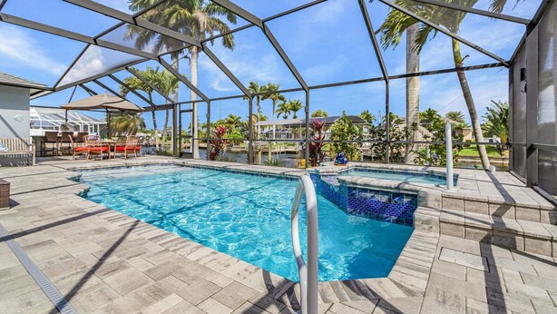 Zona de piscina con estructura de cristal, palmeras y zona de barbacoa.