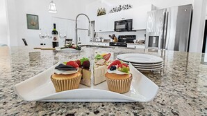 Una cocina moderna con encimera de granito, electrodomésticos de acero inoxidable y una zona de comedor con mesa y sillas blancas.