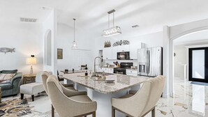 Una cocina moderna con una isla central, armarios blancos, electrodomésticos de acero inoxidable y suelo de mármol.