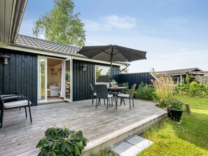 A wooden deck with outdoor furniture, a sliding glass door leading to a room, and a garden area with plants. - "Nikica" -  from the sea by Interhome (Hadsund)