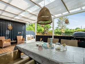 An outdoor dining area with wicker furniture, a table set with plates and glasses, and a hanging wicker light fixture. - "Nikica" -  from the sea by Interhome (Hadsund)