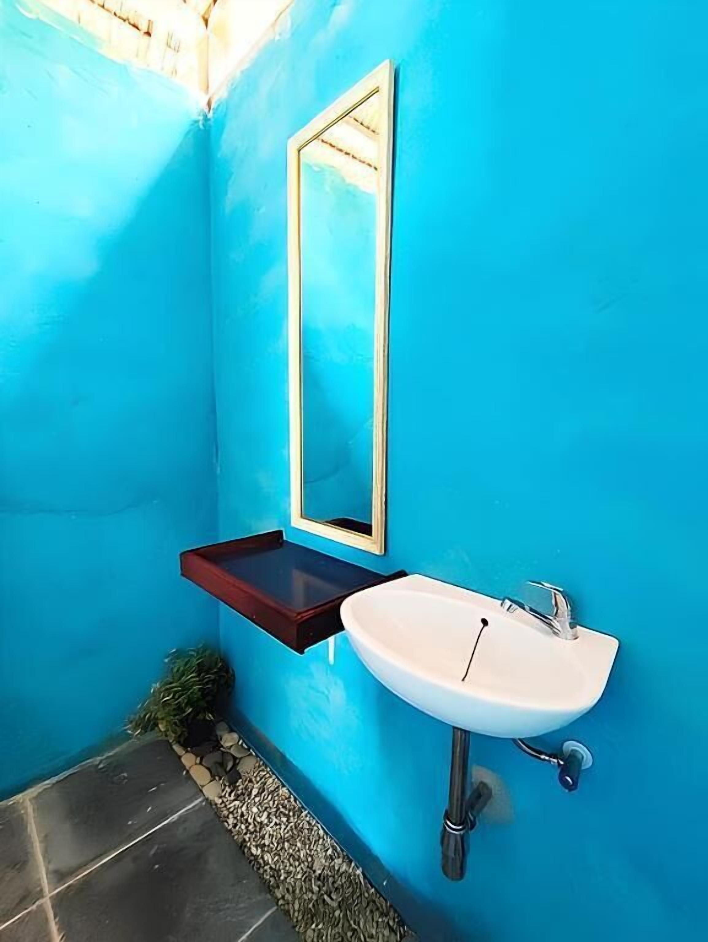 Une salle de bain avec un mur bleu, un lavabo blanc, un miroir et une petite étagère.