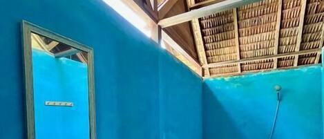 Une salle de bain avec un mur bleu, un plafond en bois, un lavabo, des toilettes et un miroir.