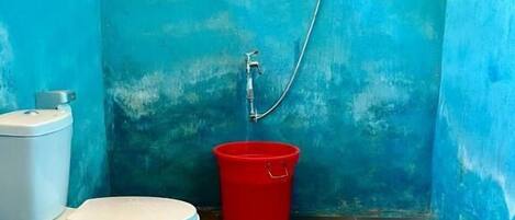 Un baño con inodoro, un cubo rojo y ducha.
