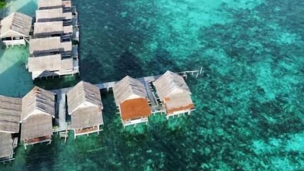 Vue aérienne de bungalows sur pilotis, avec une eau turquoise cristalline et une végétation luxuriante.
