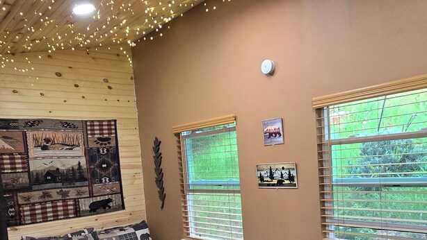 A cozy bedroom with a bed, a fireplace, a window with blinds, and a ceiling with string lights.