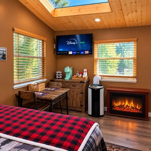 Ein gemütliches Zimmer mit Kamin, einem Fernseher, der Disney+ und Hulu zeigt, einer Kaffeestation und einem Bett mit kariertem Überwurf.
