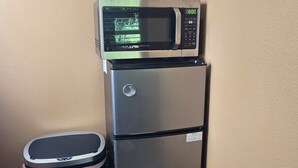 A kitchenette with a microwave, refrigerator, trash bin, and a fire extinguisher on the wall.