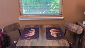 A dining table with two chairs, a window with blinds, and a picture on the wall.