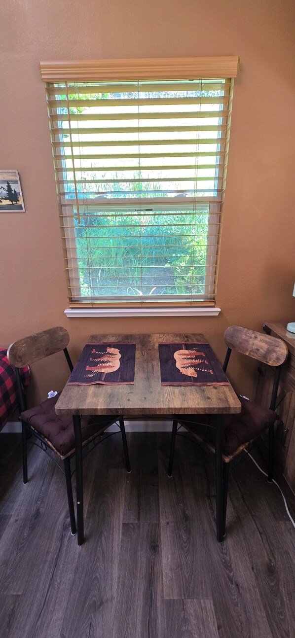 A dining table with two chairs, a window with blinds, and a picture on the wall.