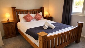 Ein hölzernes Himmelbett mit einer dunkelblauen Bettdecke, zwei Zierkissen, einem aufgerollten weißen Handtuch und zwei Nachttischlampen.