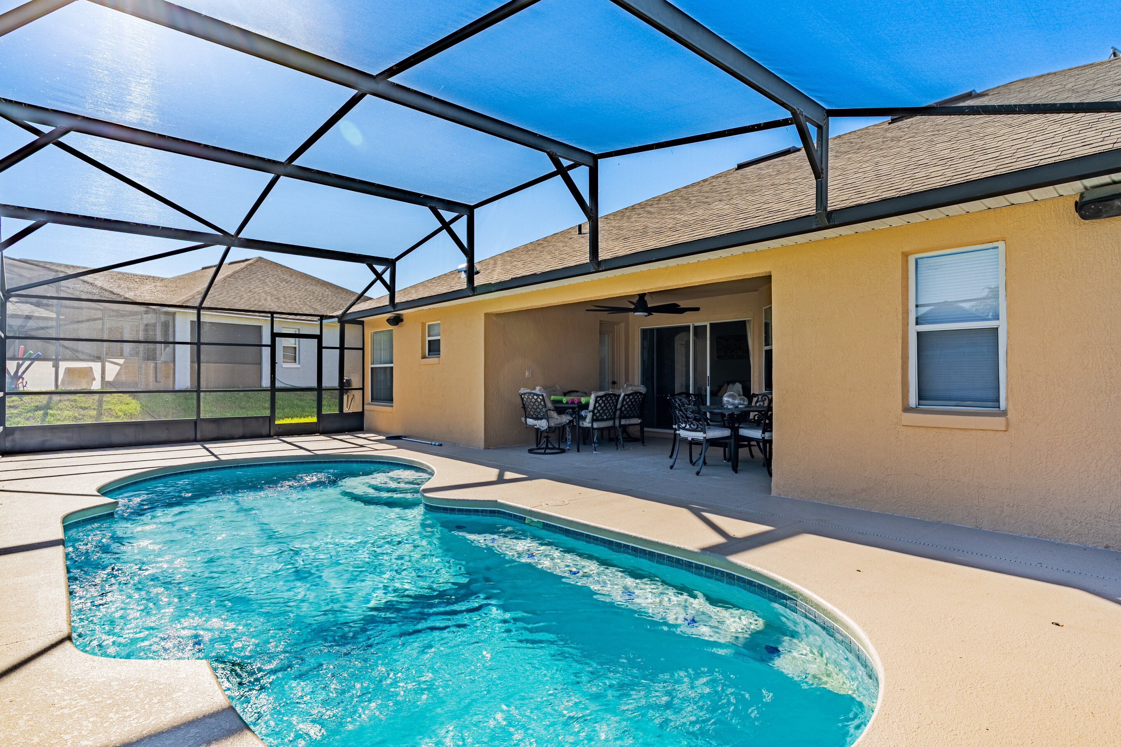 A swimming pool with a glass enclosure, outdoor furniture, and a clear sky.