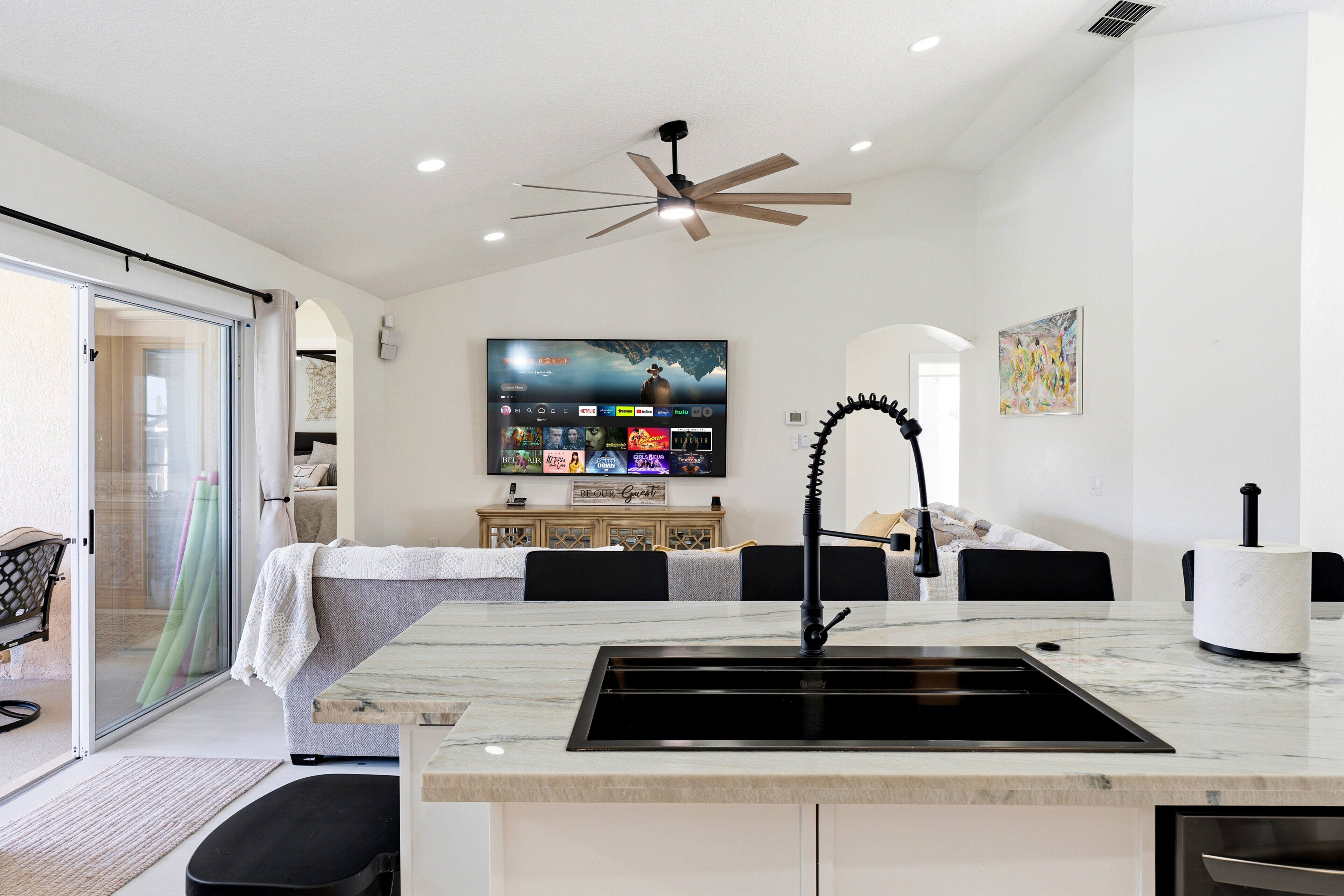 A modern kitchen with a marble countertop, black sink, and a ceiling fan.