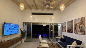 A modern living room with a flat-screen TV, a dining table with salt and pepper shakers, and a sofa. - New - Modern Coastal Villa, Walk To Beach (Port Elizabeth)
