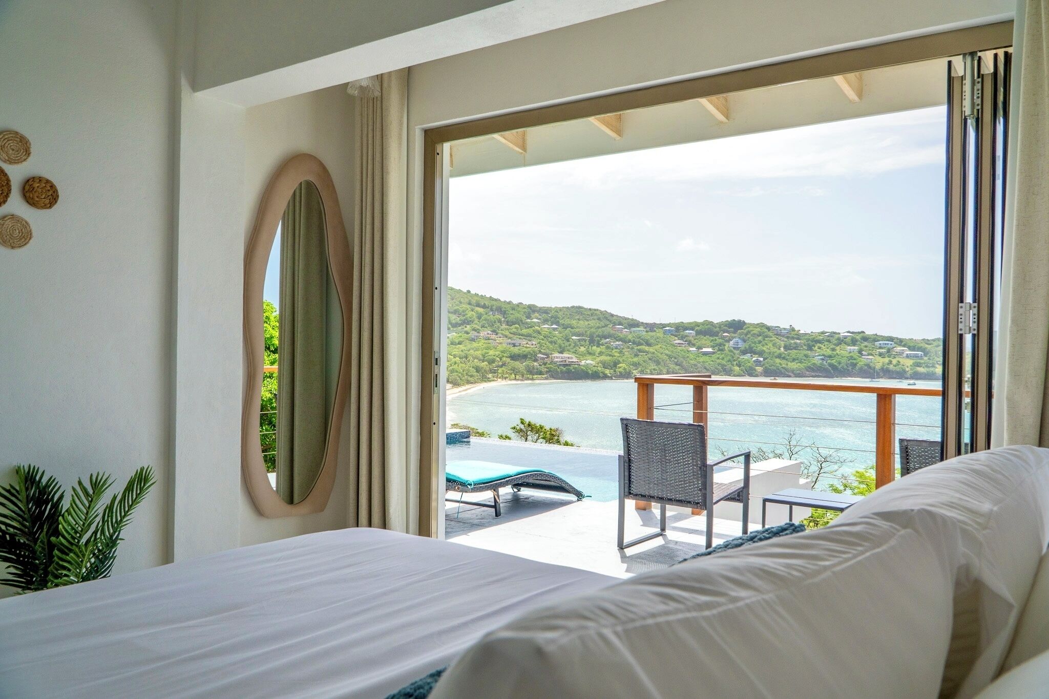 Habitación de hotel con cama, ventana grande, vista a la playa y balcón con una silla y una mesa.