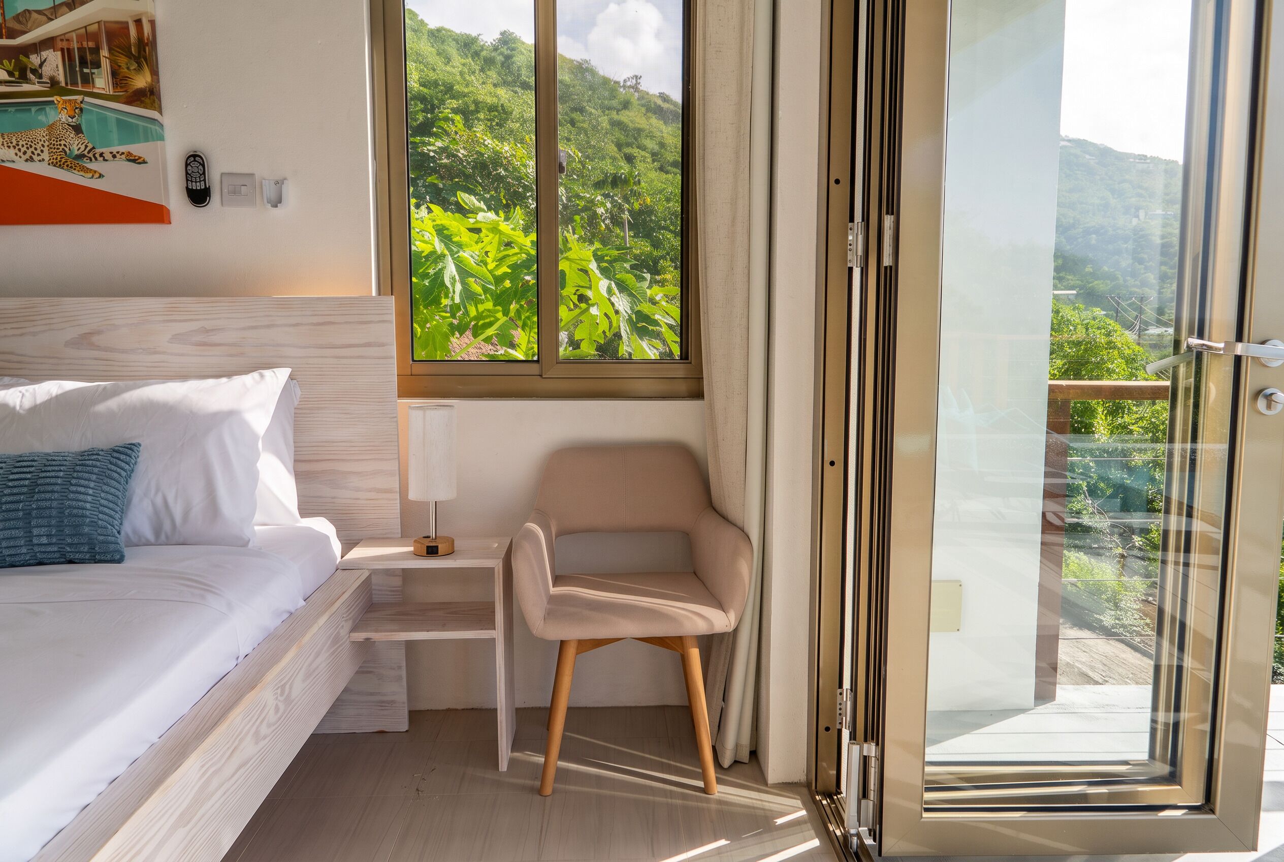 Une chambre à coucher comprenant un lit, une chaise, une table de chevet, une lampe et une grande fenêtre donnant sur un paysage verdoyant.