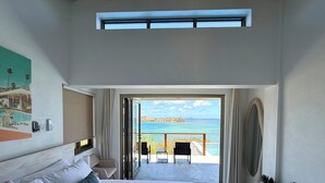 Een slaapkamer met een groot bed, een schilderij, een telefoon en uitzicht op de zee door een geopende deur.