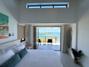 Une chambre à coucher avec un grand lit, un tableau, un téléphone et une vue sur la mer par une porte ouverte.