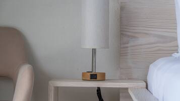 A bedside table with a lamp, a chair, and a bed in a hotel room.