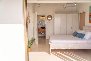 A bedroom with a bed, a wardrobe, a mirror, and a potted plant.