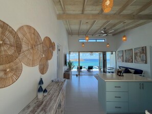 En modern inredning med ett träpanelat tak, ett köksområde med ett blått skåp och utsikt över havet genom en glasdörr.