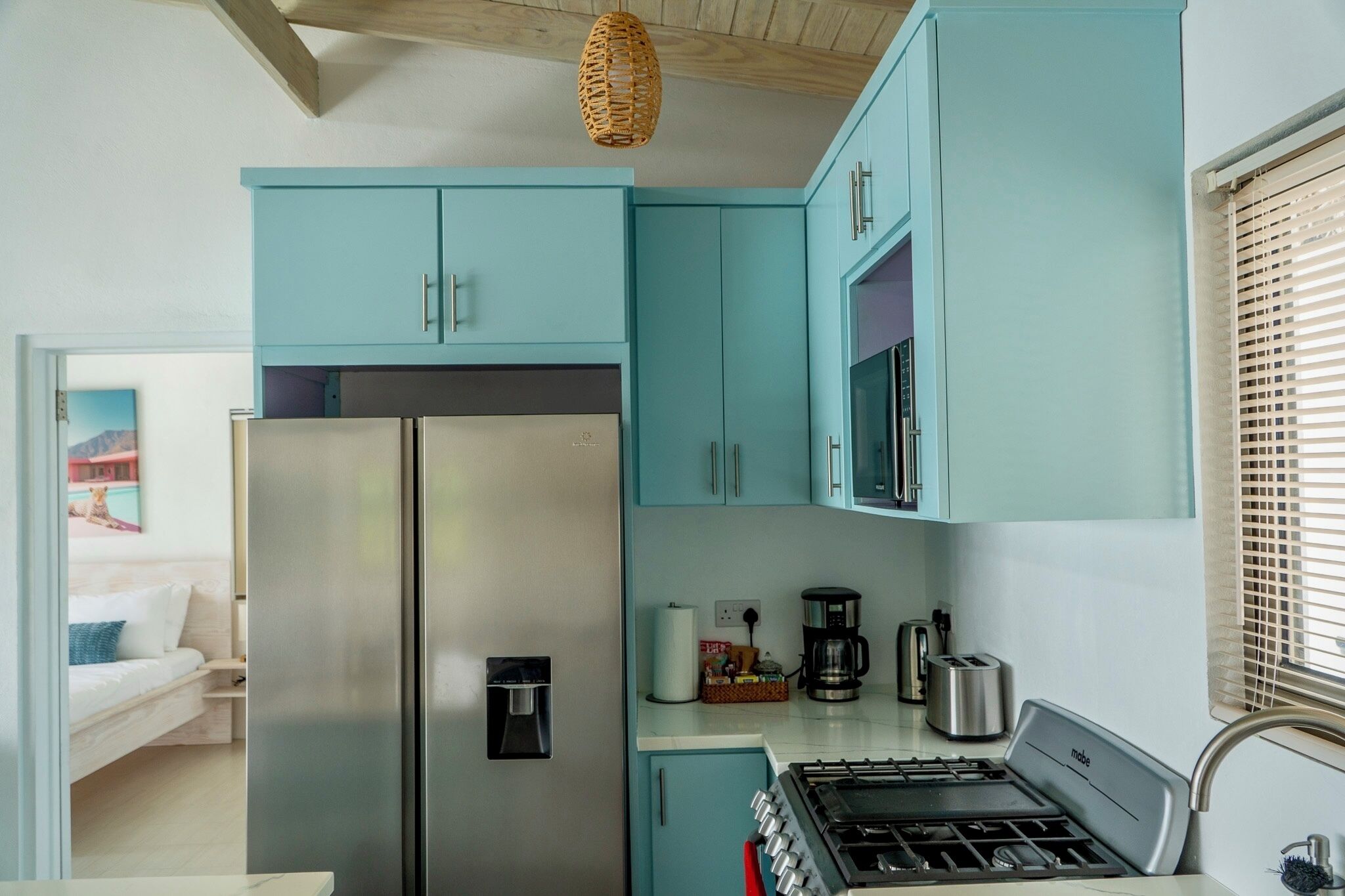 A compact kitchen with teal cabinets, a stainless steel refrigerator, a coffee maker, and a gas stove.
