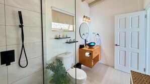 Een badkamer met een douchecabine van glas, toilet, wastafel met spiegel en een witte deur.