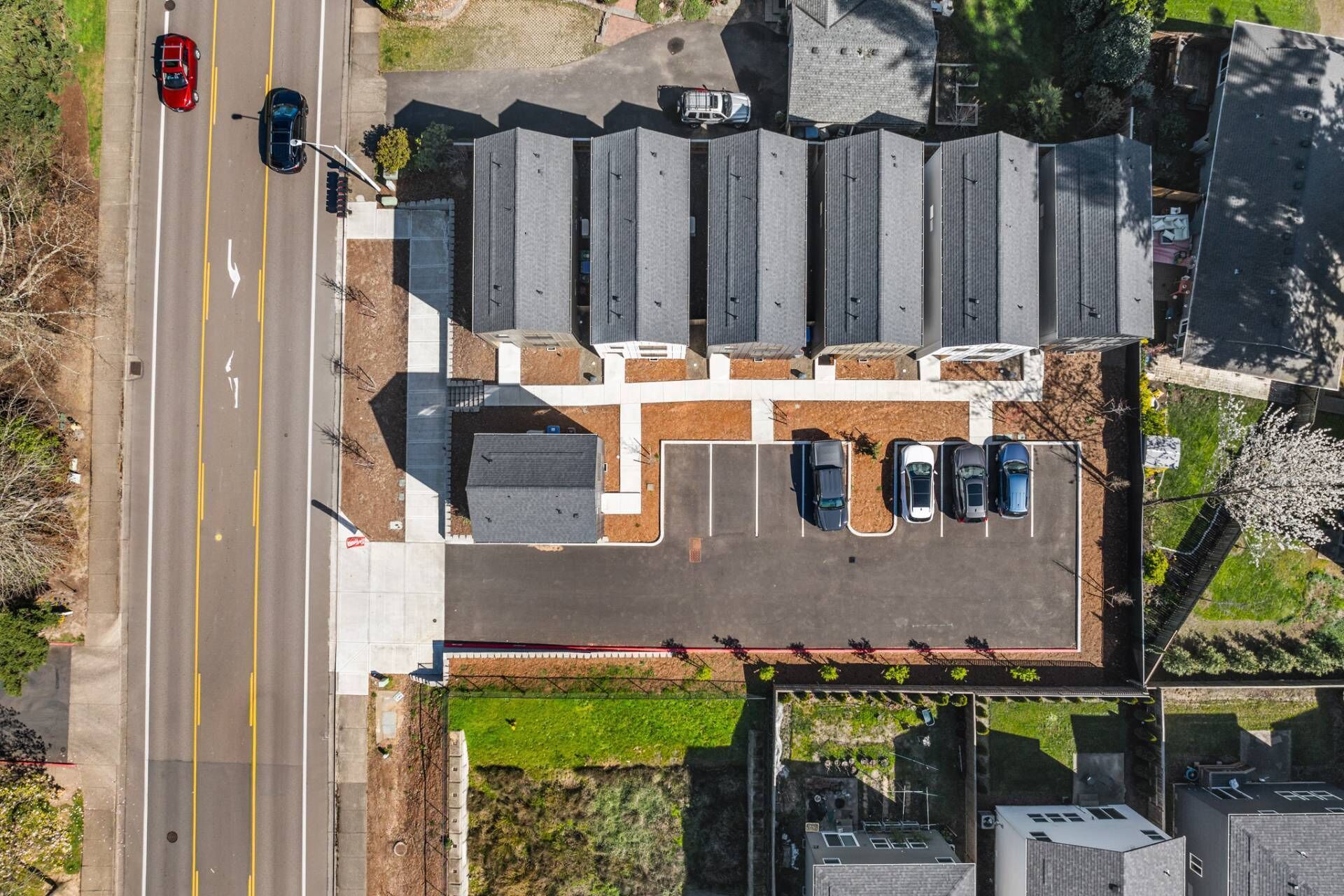 An aerial view of a parking lot with multiple cars, a road with a traffic light, and buildings with flat roofs.