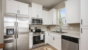 A modern kitchen with stainless steel appliances, white cabinetry, and a window with blinds. - Chiquita Bonita | Brand New, Stylish & Spotless, Pet Friendly, Walk to Park, Minutes from Downtown (Tigard)
