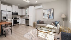 A modern kitchen with white cabinets, stainless appliances, and a dining area with a wooden table and chairs. - Chiquita Bonita | Brand New, Stylish & Spotless, Pet Friendly, Walk to Park, Minutes from Downtown (Tigard)
