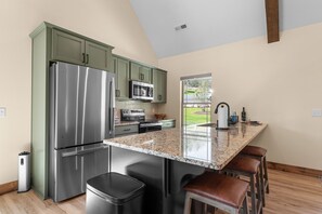 A kitchen with a stainless steel refrigerator, microwave, and oven, green cabinets, a granite countertop, and a window with a view of greenery. - Tall Timbers Cabin Right Across Community Pools_Free Daily Tickets_Near Thunder Ridge (Hollister)