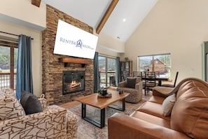 Amplia sala de estar con chimenea de piedra, asientos cómodos y ventanas grandes con vistas al exterior.