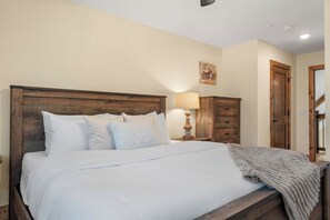 Un lit bien fait, avec du linge de lit blanc et des oreillers, une tête de lit en bois, une lampe de chevet et une armoire en bois.