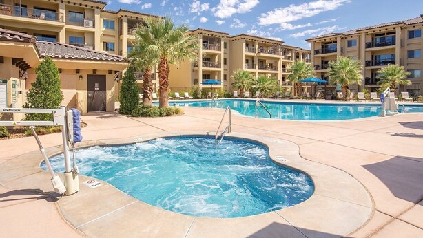 A hotel with a swimming pool, palm trees, and a clear blue sky. - Spacious 4-master-suite condo in charming St. George (St. George)