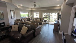 A spacious living room with multiple leather sofas, a ceiling fan, and large windows offering a view of the outside. - Spacious 4-master-suite condo in charming St. George (St. George)