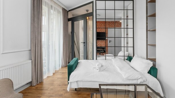 Ett modernt hotellrum med en säng, ett soffbord i glas, en fåtölj med fiskbensmönster och utsikt över en tegelvägg och en tv.