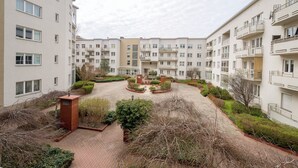 A multi-story residential building with balconies, a central courtyard with greenery, and a brick pathway.