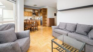 A modern living room with a sofa, a glass coffee table, and a dining area with wooden furniture.
