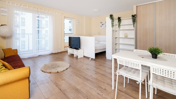 Ein modernes Wohnzimmer mit einer Couch, einem Fernseher, einem Esstisch mit Stühlen und einem weißen Kleiderschrank.