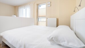 Ein Schlafzimmer mit einem Bett, einem Heizkörper, einem Fenster mit Jalousien und einer Wand-Klimaanlage.