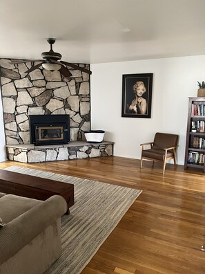 A living room with a stone fireplace, a framed portrait, a bookshelf, and a brown leather chair. - Spacious 3-bedroom House Central to all of SoCal (Lakewood)