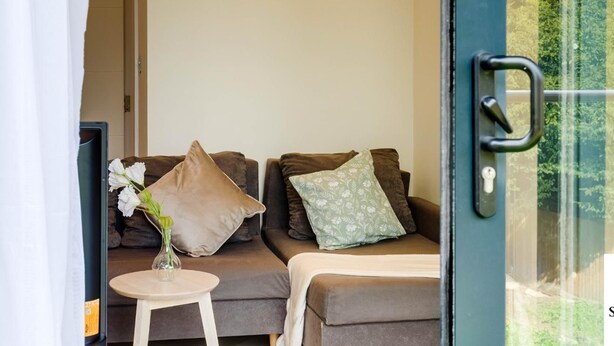Une pièce comprenant un canapé, une petite table ornée d’un vase de fleurs et une porte donnant sur un espace extérieur.