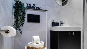 Une salle de bain moderne comprenant des toilettes, un lavabo, un meuble noir, un distributeur de papier toilette fixé au mur et une plante décorative.
