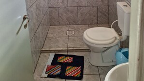 A bathroom with a toilet, a shower area, and a small shelf with toiletries.