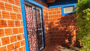 A brick building with a blue door and a window, surrounded by a garden.