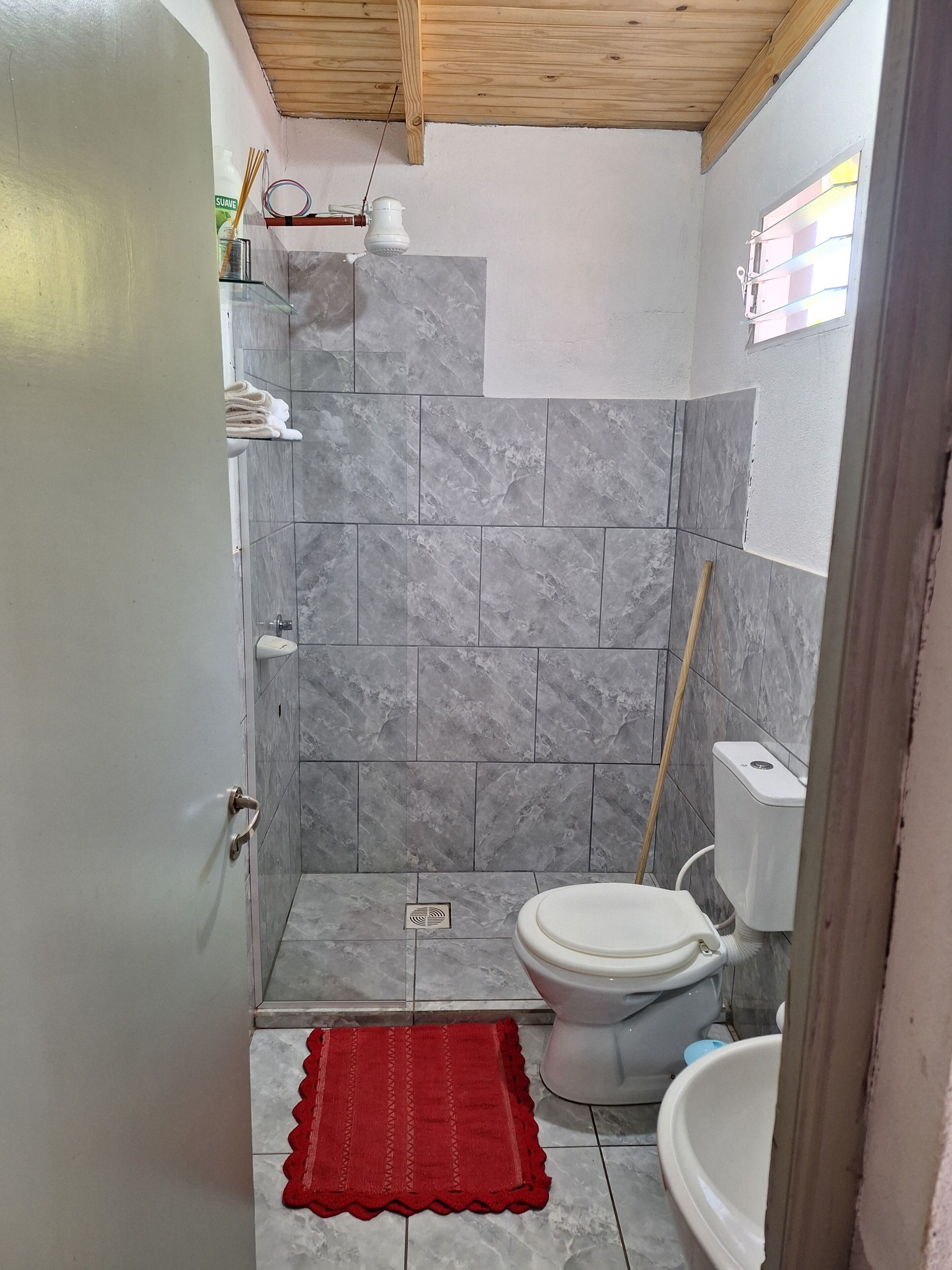 Ein Badezimmer mit grauen Marmorfliesen, einer weißen Toilette und einer roten Badmatte.
