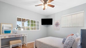 A bedroom with a bed, a desk with a mirror, a ceiling fan, a TV, and a window. - Moroccan Hacienda Retreat- By Festival Grounds (Indio)