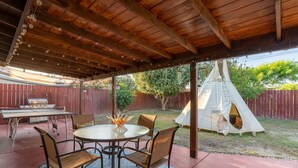 A covered patio with a round table and chairs, a barbecue grill, and a tent in the background. - Moroccan Hacienda Retreat- By Festival Grounds (Indio)